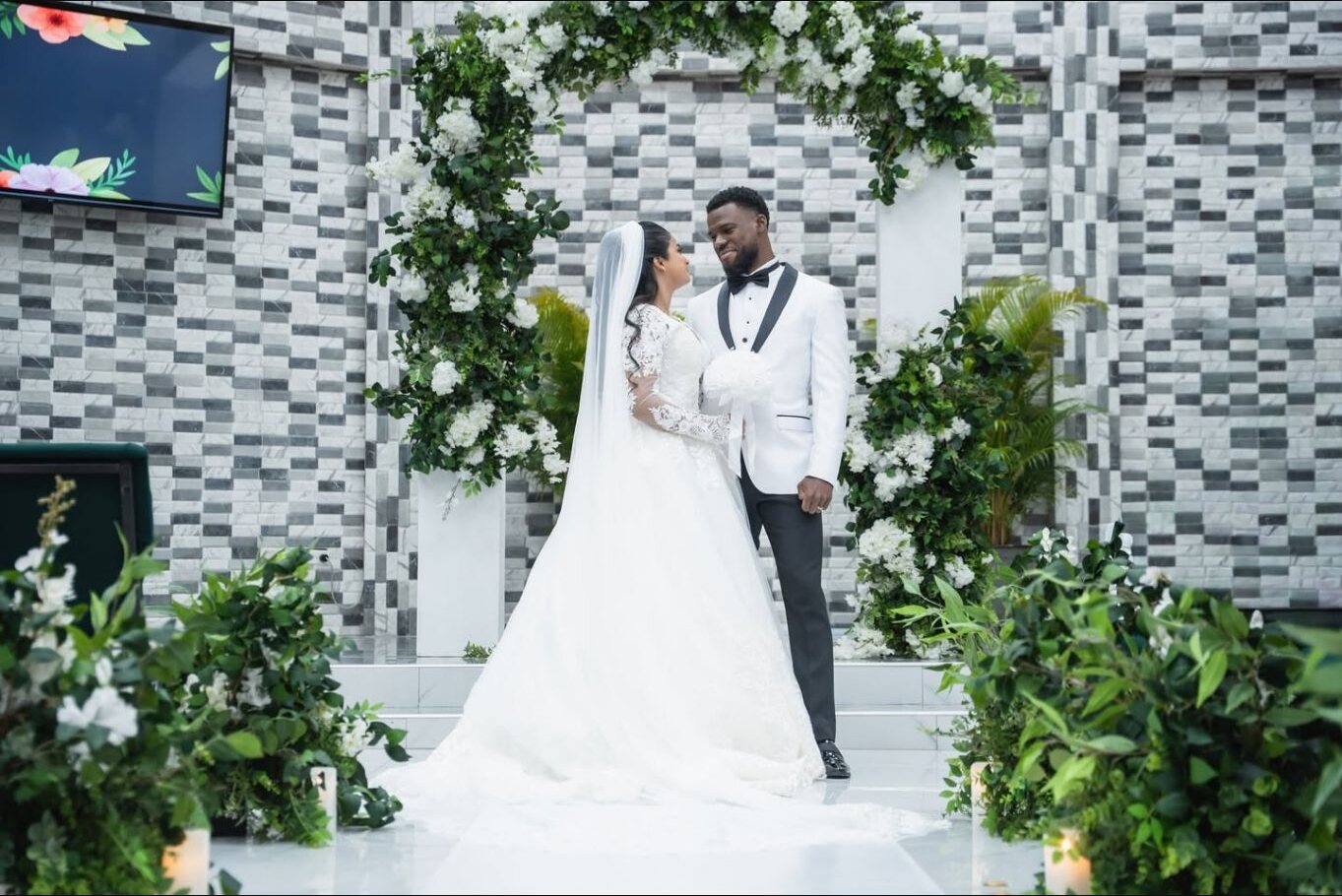 Newlyweds looking at one another beneath a floral ceremony arch