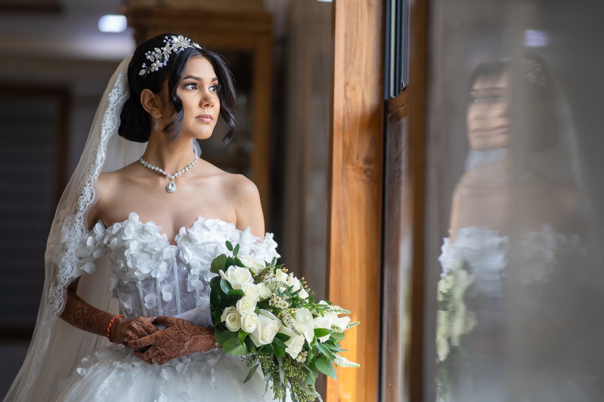 Bride holding white flowers beside a window